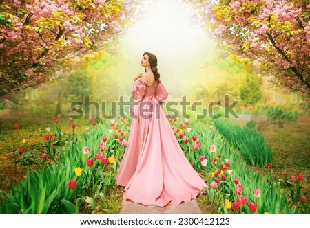 Fantasy girl princess walks in blooming spring garden flowers tulips sakura tree green grass old alley. Woman queen in long luxurious royal pink dress with train puffed sleeves vintage style art photo Royalty-Free Stock Photo #2300412123
