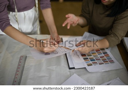 Two professional female fashion designers or dressmakers discussing and checking new model sketches in the studio together. cropped image