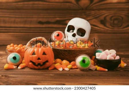 Halloween pumpkin-flavored corn candy, jelly eye, sugar skull and jelly beans on a brown background. Classic sweet Halloween treats. Halloween holiday concept and Jack lantern.Place for text. 