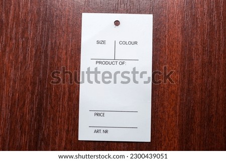 Blank white carton clothing swing tag in the form of the rectangular carton sheet with hole lies on the red wooden table, top view 
