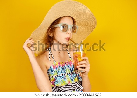 Child teenager girl in swimsuit, straw hat and sunglasses with lemonade metal straw in studio on yellow background, summer mood, Royalty-Free Stock Photo #2300441969
