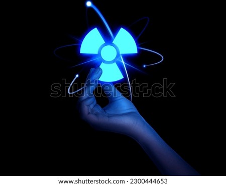 Woman holding glowing atom symbol with radiation warning sign on black background, closeup