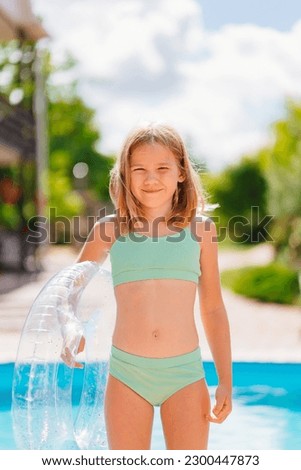 Cute and funny blonde teenage girl in a swimsuit with an inflatable lifebuoy near the pool. Safe rest with children by the water. travel and tourism. Royalty-Free Stock Photo #2300447873