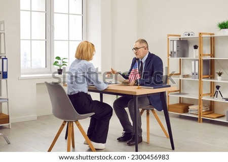 Government authority or United States of America embassy consul discusses visa application with customer at table in office. Male Immigration Services agency worker meeting with woman who moved to USA Royalty-Free Stock Photo #2300456983