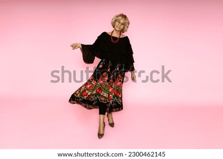 Happy mother's day! Beautiful happy senior woman in folk floral skirt on pink background in studio.