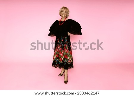 Happy mother's day! Beautiful happy senior woman in folk floral skirt on pink background in studio.