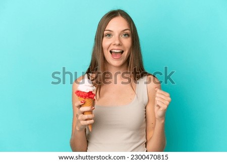Young Lithuanian woman with cornet ice cream isolated on blue background celebrating a victory in winner position