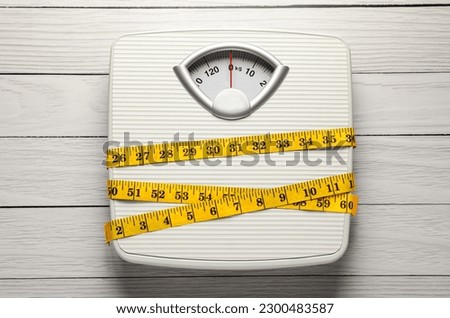 Weigh scales tied with measuring tape on white wooden table, top view. Overweight concept