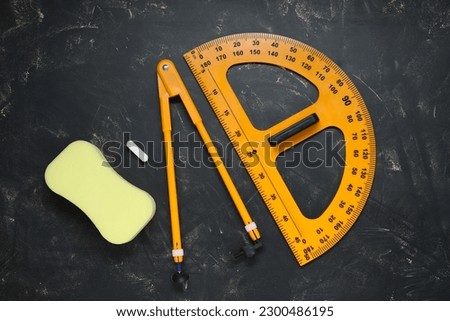Protractor, compass, chalk and sponge on blackboard, flat lay