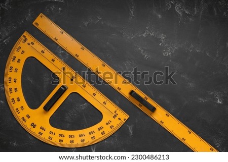Ruler and protractor with measuring length and degree markings on blackboard, flat lay. Space for text