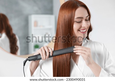 Beautiful woman using hair iron in room, space for text Royalty-Free Stock Photo #2300490031