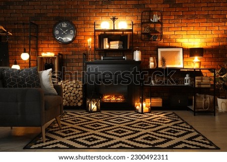 Stylish living room with beautiful fireplace, armchair and different decor at night. Interior design