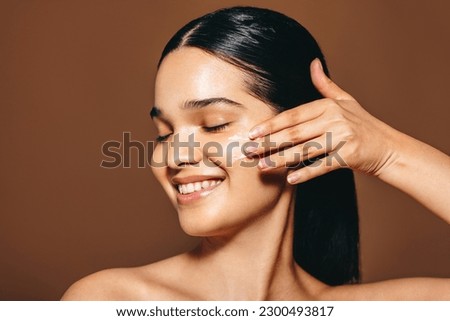 Young woman with perfect skin applies facial cream, she smiles as she makes use of this beauty product with is an essential part of her daily skincare routine. Woman in her 20’s caring for her skin. Royalty-Free Stock Photo #2300493817