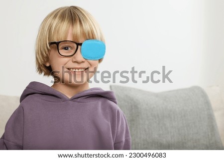 Happy boy with nozzle on glasses for treatment of strabismus in room. Space for text Royalty-Free Stock Photo #2300496083
