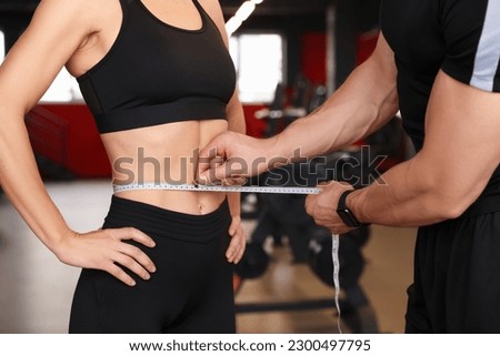 Trainer measuring woman`s waist with tape in gym, closeup