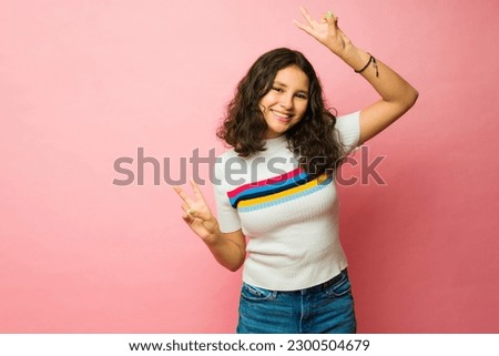 Hispanic thirteen year old teen girl feeling happy making the peace sign and having fun next to pink copy space