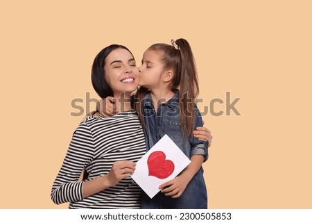 Happy woman with her cute daughter and handmade greeting card on beige background, space for text. Mother's day celebration
