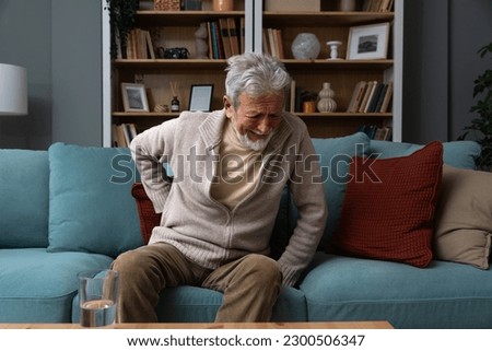 Aged grey haired senior red face man writhes in pain suffers from low back strain, touch rubbing or massaging loin reduces backache. Degenerative disk disease, pinched nerve rheumatism concept Royalty-Free Stock Photo #2300506347