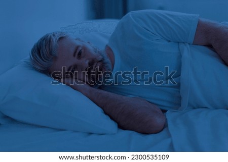 Awake sleepless upset middle aged man lying in bed alone at night, cant sleep, feeling lonely, suffering from depression or anxiety, experiencing difficulties with sleeping, home interior Royalty-Free Stock Photo #2300535109