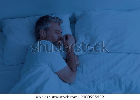 Top view of single handsome grey-haired middle aged man wearing pajamas peacefully sleeping alone in bed at night at home, empty pillow and free space next to him Royalty-Free Stock Photo #2300535159