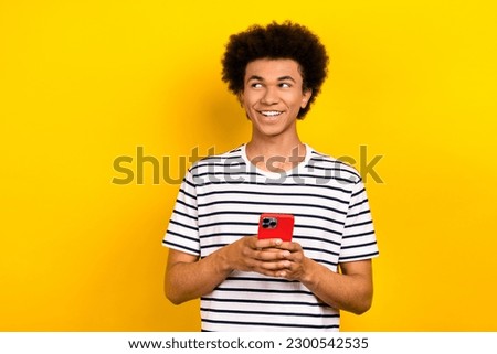 Photo of youth positive guy wear striped t-shirt hold smartphone looking empty space searching web page isolated on yellow color background