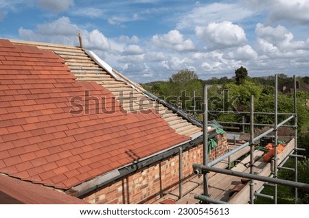 Red clay roof tiles being laid on a residential property in northwest London. Royalty-Free Stock Photo #2300545613