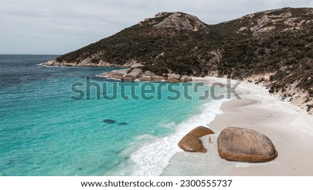 Aerial picture. Girl at the beach going for a swim with orange swimsuit. Ocean view from the sky, beautiful landscape located in Little beach, Albany, Australia. Big rock in the middle of the beach.