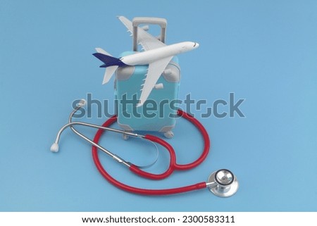 Airplane model on suitcase and red stethoscope on blue background. Travel insurance, medical tourism and healthcare concept. Royalty-Free Stock Photo #2300583311
