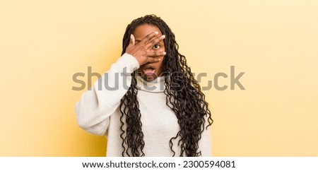 black pretty woman looking shocked, scared or terrified, covering face with hand and peeking between fingers Royalty-Free Stock Photo #2300594081