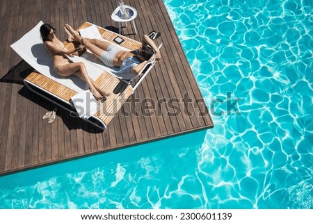 Couple laying on lounge chair at poolside Royalty-Free Stock Photo #2300601139