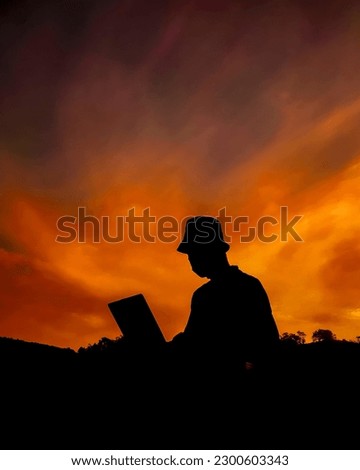 silhouette of a person opening a laptop against a sky background
