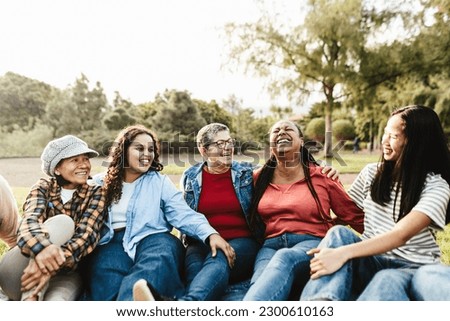 Happy multi generational group of women with different ethnicities having fun sitting on grass in a public park - Females empowerment concept Royalty-Free Stock Photo #2300610163