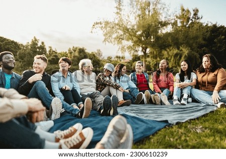 Happy multi generational people having fun sitting on grass in a public park - Diversity and friendship concept Royalty-Free Stock Photo #2300610239