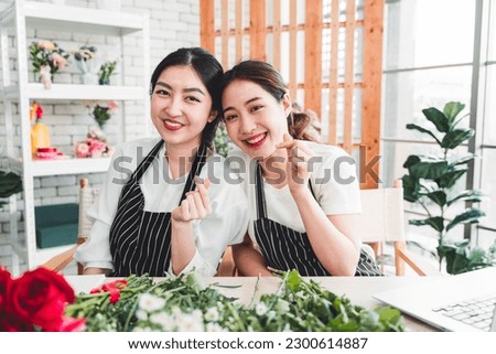 Young female florist taking pictures to promote the shop two girls making miniheart hand and bright smiling faces in a flower shop full of flowers.