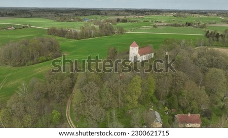  an aerial view of a church surrounded by green fields and a wooded area in the distance, with a train track running through the center of the picture. . 