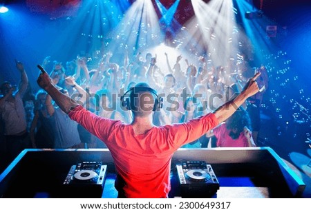 Dj with arms outstretched overlooking dance floor Royalty-Free Stock Photo #2300649317