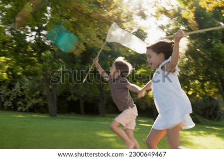 Happy boy girl holding hands running with butterfly nets in grass
