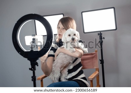 Romantic photo of a dog in the warm embrace of its owner. Friends forever. Blank empty space, colorful room and lighting background. Radio host, charming influencer girl, records a live show.