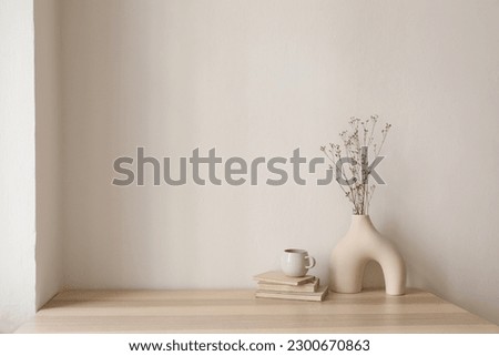 Elegant interior still life. Modern organic, geometric shaped vase with dry flowers, grass. Pile of old books, cup of coffee on wooden table. Home staging, minimal decor concept. Blank beige wall. Royalty-Free Stock Photo #2300670863