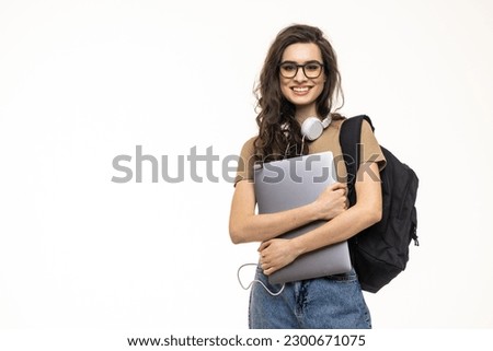 Portrait of a pretty girl carrying backpack standing isolated over white background, holding laptop computer
