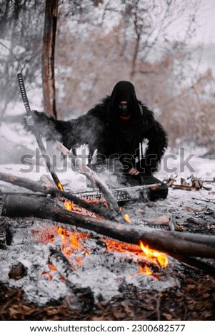 Surrealism theme: a man in a hannya mask, black kimono, and a katana in his hands in a winter forest. Surrealistic image of a man in a hannya half mask, kimono with a katana. Surreal samurai, ninja Royalty-Free Stock Photo #2300682577