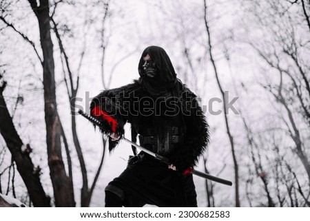 Surrealism theme: a man in a hannya mask, black kimono, and a katana in his hands in a winter forest. Surrealistic image of a man in a hannya half mask, kimono with a katana. Surreal samurai, ninja Royalty-Free Stock Photo #2300682583