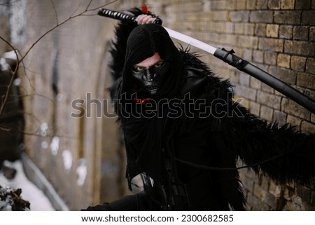 Surrealism theme: a man in a hannya mask, black kimono, and a katana in his hands in a winter forest. Surrealistic image of a man in a hannya half mask, kimono with a katana. Surreal samurai, ninja Royalty-Free Stock Photo #2300682585