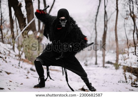 Surrealism theme: a man in a hannya mask, black kimono, and a katana in his hands in a winter forest. Surrealistic image of a man in a hannya half mask, kimono with a katana. Surreal samurai, ninja Royalty-Free Stock Photo #2300682587
