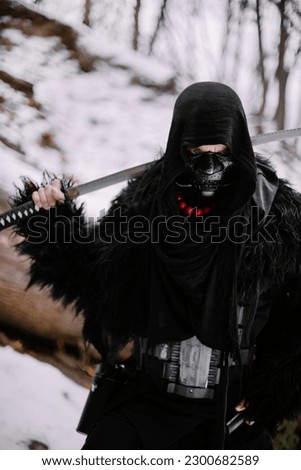 Surrealism theme: a man in a hannya mask, black kimono, and a katana in his hands in a winter forest. Surrealistic image of a man in a hannya half mask, kimono with a katana. Surreal samurai, ninja Royalty-Free Stock Photo #2300682589