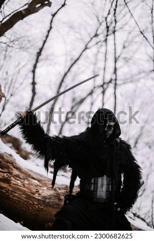Surrealism theme: a man in a hannya mask, black kimono, and a katana in his hands in a winter forest. Surrealistic image of a man in a hannya half mask, kimono with a katana. Surreal samurai, ninja Royalty-Free Stock Photo #2300682625