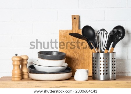 Kitchen table, kitchen utensils, plates, bowls, shakers and wooden cutting board. Royalty-Free Stock Photo #2300684141