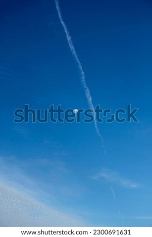 Blue sky with cloud in Brazil, with moon in the background and white condensation trail (contrail) of airplane