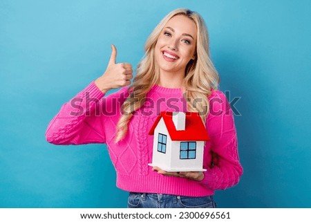 Photo of cheerful person with curly hairdo dressed knit sweater hold house showing thumb up approve isolated on blue color background