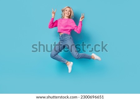 Full length cadre of smiling happy woman jumping show double v-sign wear jeans and sweater casual look isolated on blue color background